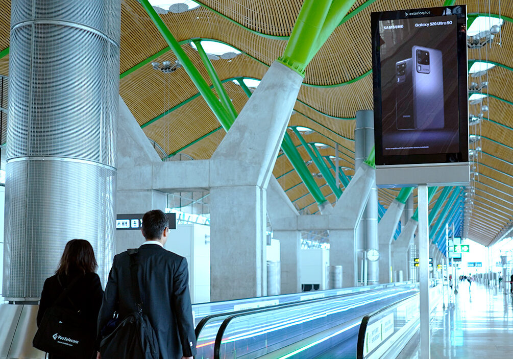 Modern airport terminal with a moving walkway, giant metal columns, and green structural beams under a wooden ceiling.